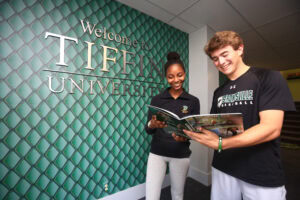 two students standing in the welcome center in front of the tiffin university sign