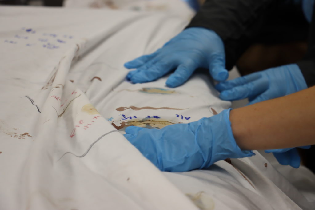 gloved hands testing stains on a sheet