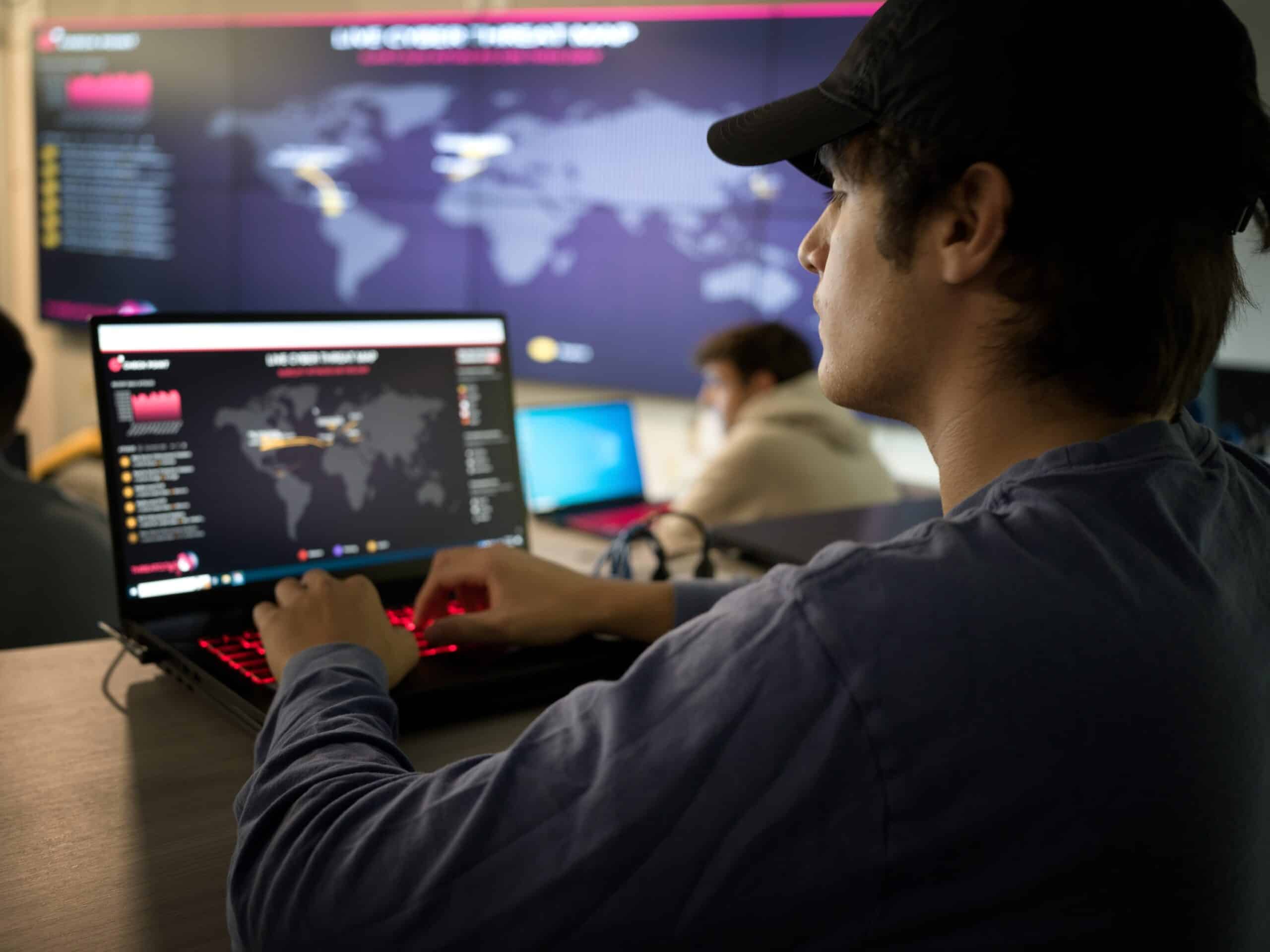 Cybersecurity student viewing live cyber threat map on laptop