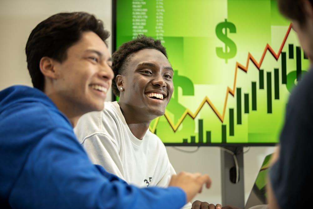 Students sitting in a clasroom with a dollar sign on a screen behind them